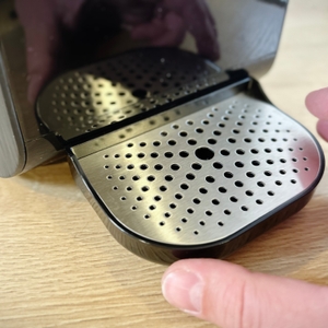 Eine Hand justiert die Tropfschale der Osmofresh Quella Pro Black unterhalb des Auslasses. Die Schale wird gerade angesetzt.