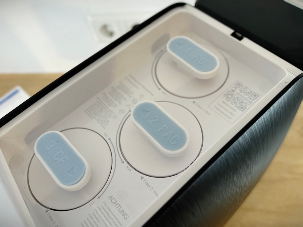 Das Bild zeigt das geöffnete Kartuschenfach der Osmofresh Quella Pro Black mit drei beschrifteten Filtern: RO, PAC und CF.