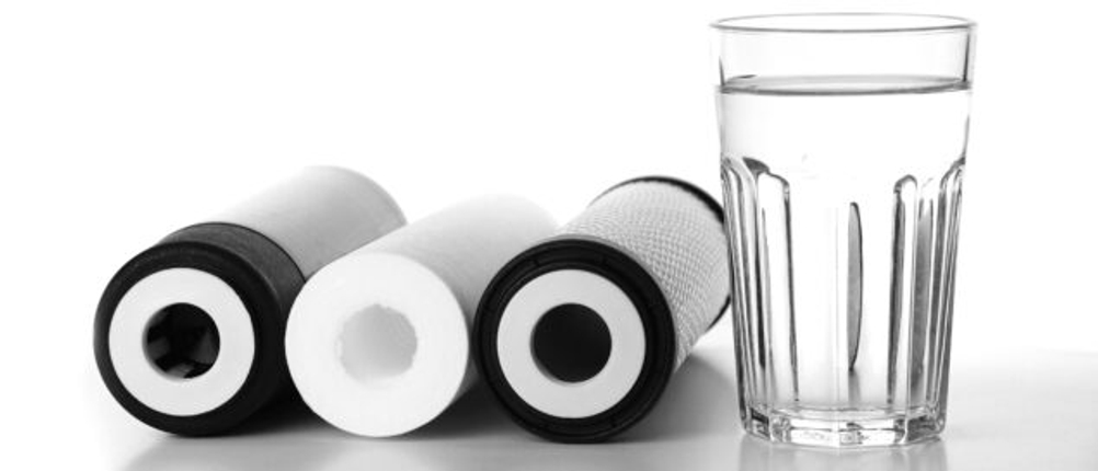 Neben einem Glas Wasser liegen drei Filter für Osmoseanlagen.