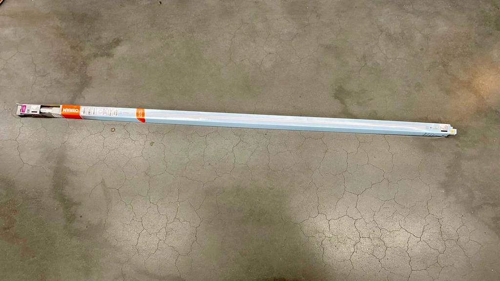 Eine LED-Röhre 120 cm liegt zum testen quer auf einem Steinboden.