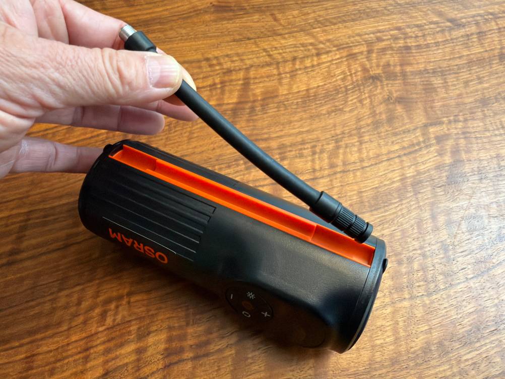 Eine Hand nimmt den Schlauch vom Osram TyreInflate 2000 aus der Halterung