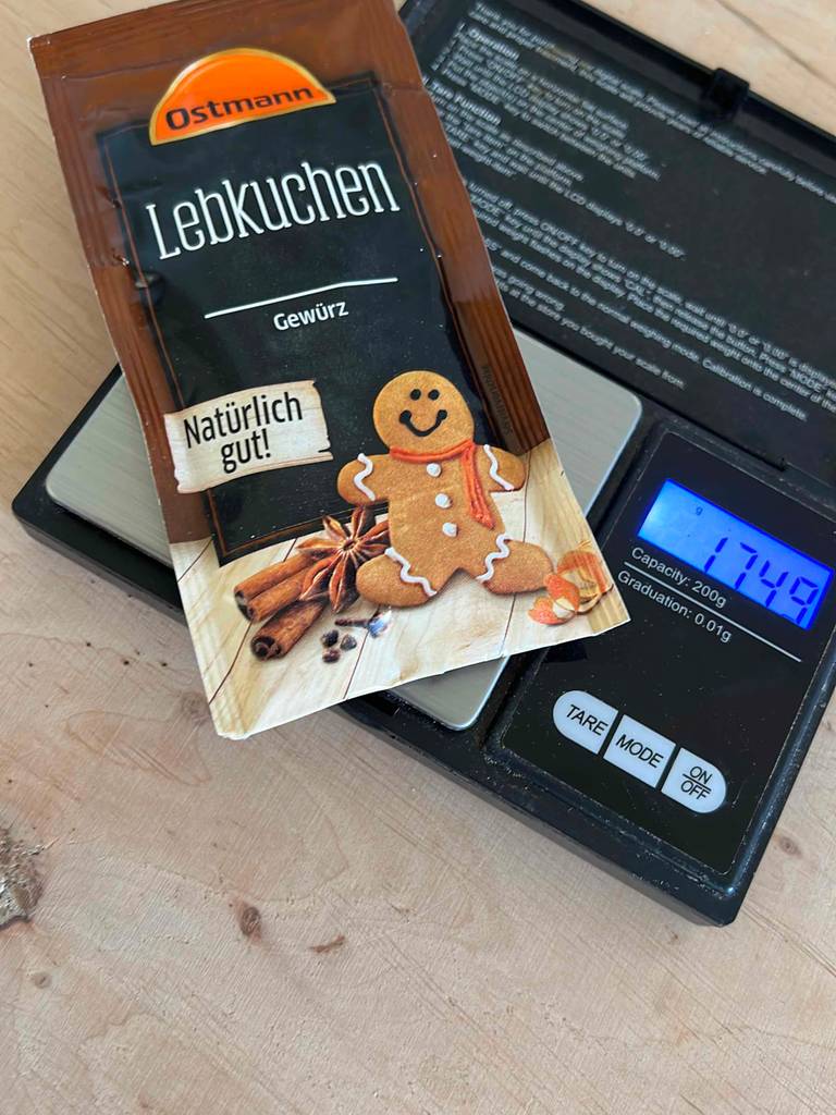 Eine Tüte Ostmann Lebkuchengewürz im Test liegt auf einer schwarzen eingeschalteten Gramm-Digitalwaage.