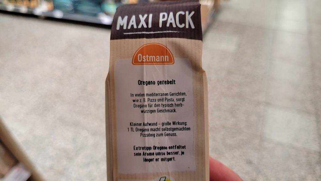Ein Maxi-Pack mit getestetem Oregano gerebelt vor einem Supermarktboden.