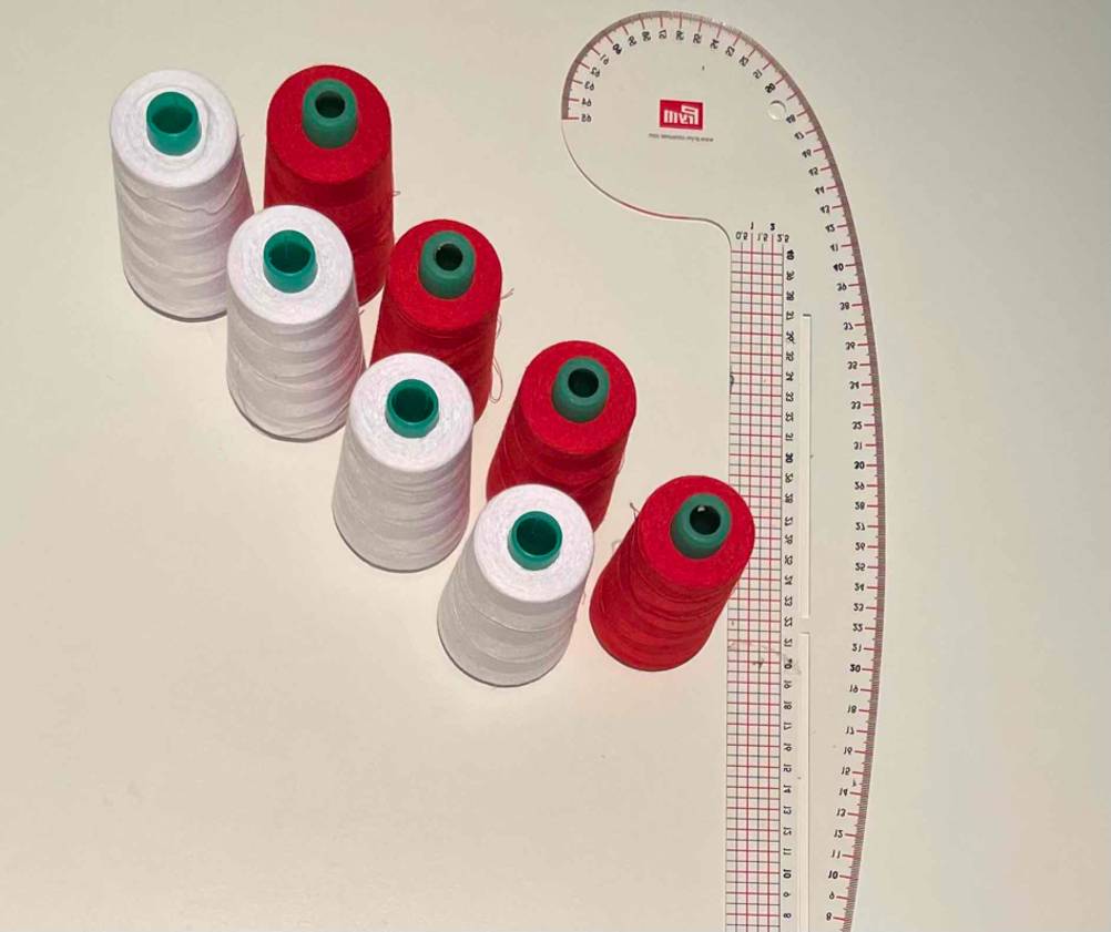 Weißes und rotes Overlockgarn im Test befindet sich neben einem Schneider-Lineal auf einem hellen Untergrund.