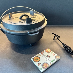 Der Overmont-Feuertopf steht neben dem Deckelheber und dem Rezeptbuch auf einer Arbeitsplatte