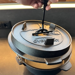 Eine Hand hebt den Deckel des Overmont-Feuertopf mit einem Deckelheber an