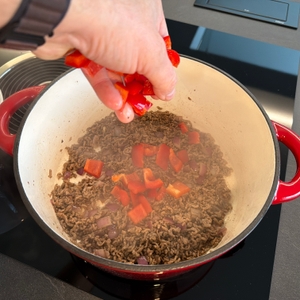 Eine Hand gibt Paprikastücke in den Overmont-Schmortopf