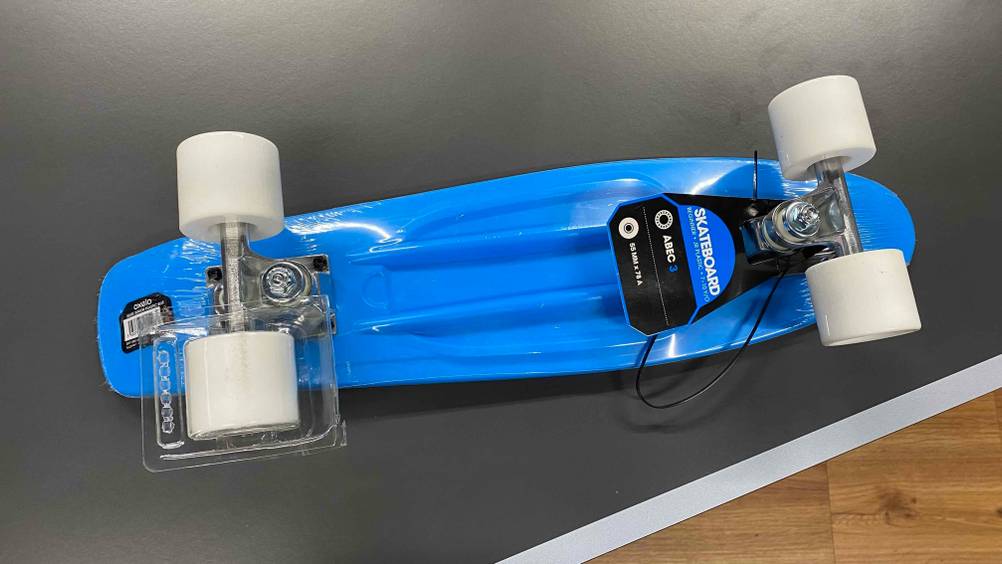 Skateboards für Kinder im Test: Unteransicht von einem blauen Modell der Marke Oxelo mit weißen Rädern auf einer grauen Fläche.
