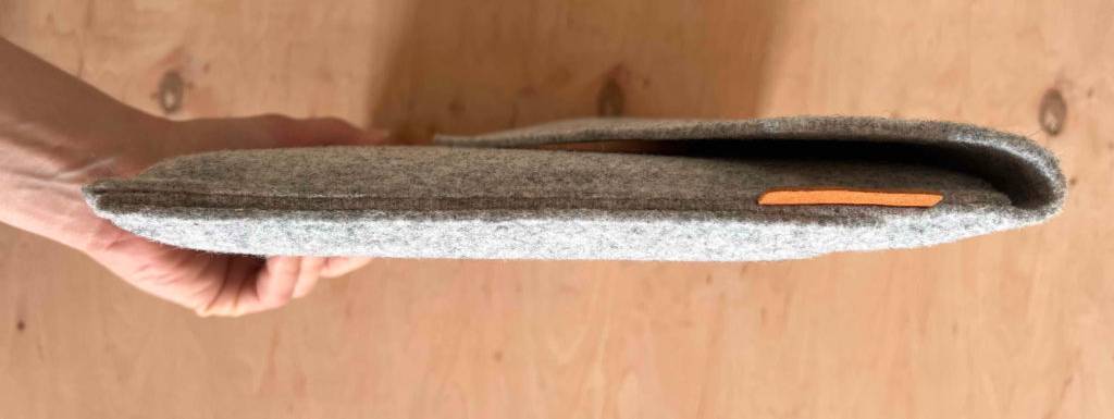 Hand hält eine getestete MacBook-Tasche aus grau melierter Wolle über einer Holzfläche mit der schmalen, langen Seite in die Kamera.