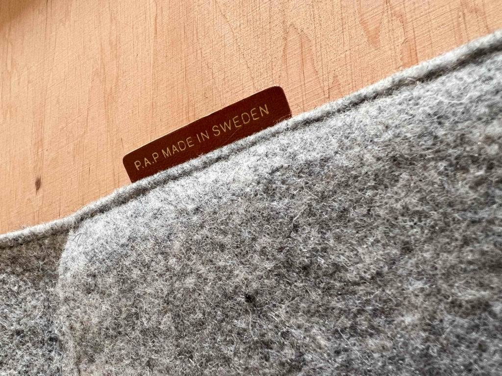 Detailansicht des grauen Wollmaterials einer getesteten MacBook-Tasche inklusive P.A.P. Made in Sweden Markenzeichen auf einem Holzuntergrund.