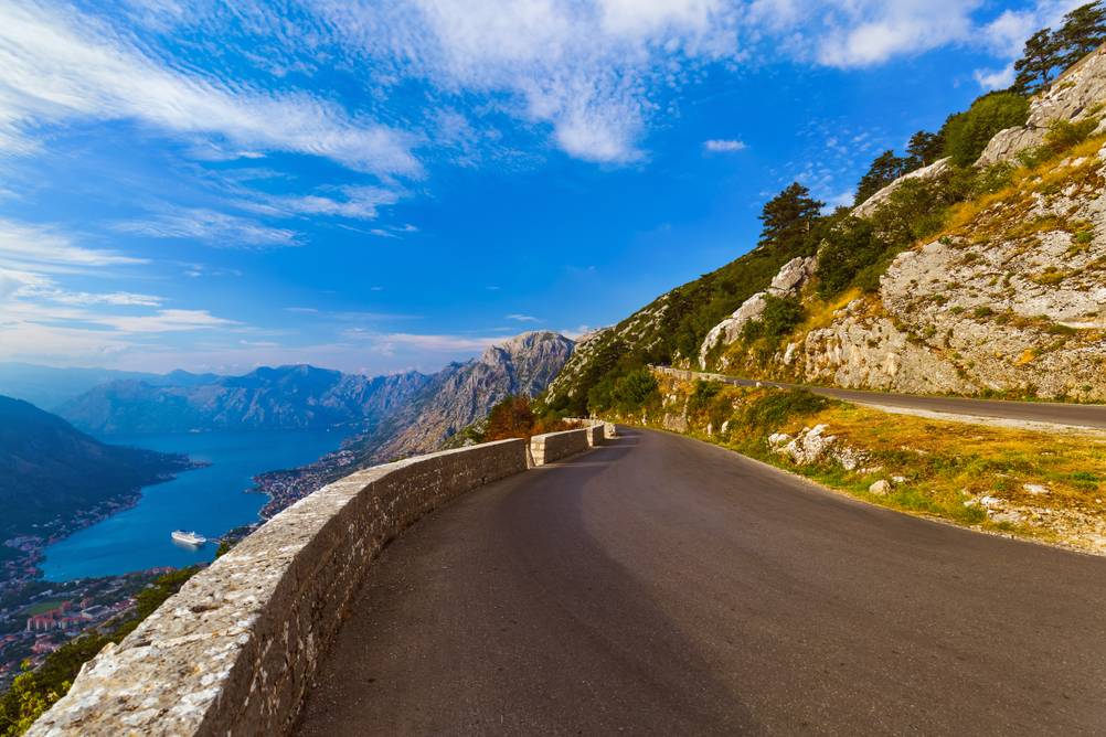 Die P1-Straße, die in einer Serpentine den Berg hinaufführt, mit Aussicht über die Bucht von Kotor an einem sonnigen Tag mit blauem Himmel.