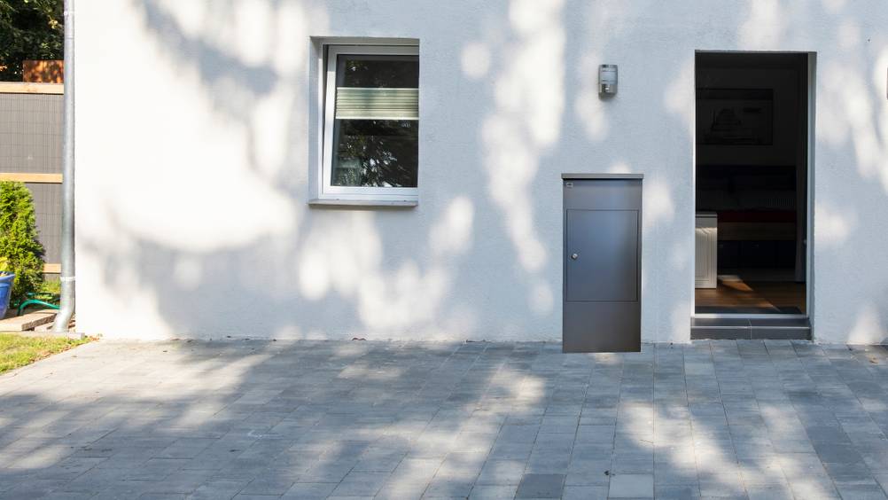 Ein getesteter Paketbriefkasten vor einem Haus mit geöffneter Tür.