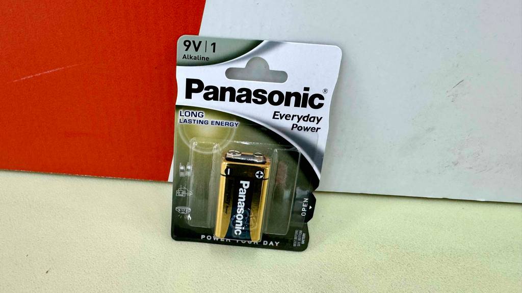 Eine getestete 9V-Batterie steht inklusive Verpackung vor einer roten Wand.