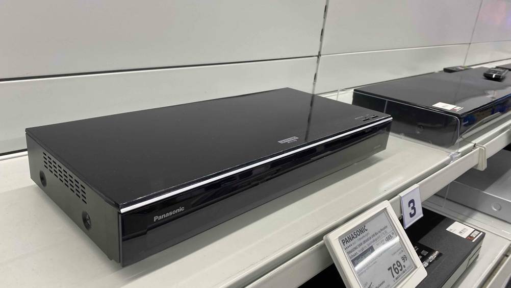 Ein getesteter Blu-ray-Recorder von schräg vorne auf einem Verkaufsregal mit einem Preisschild.