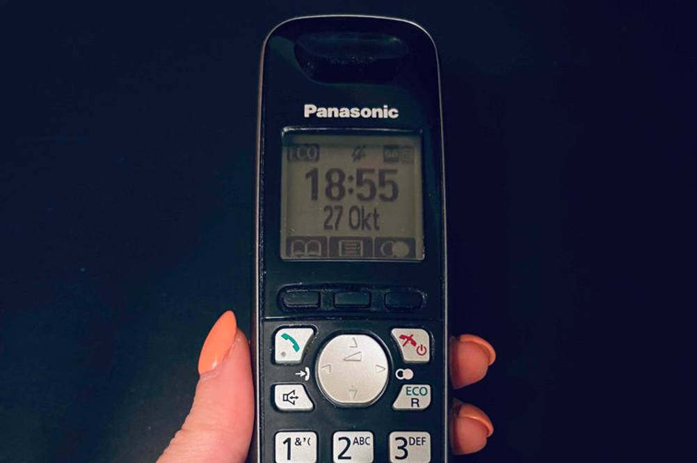Telefonanlage im Test: eine Panasonic Telefon in Schwarz-Grau in einer Hand vor einem schwarzen Hintergrund.