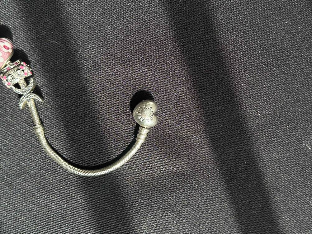 Getestet: Nahaufnahme des geschlossenen Verschlusses eines Pandora-Armbands mit Logo auf einer dunklen Fläche.