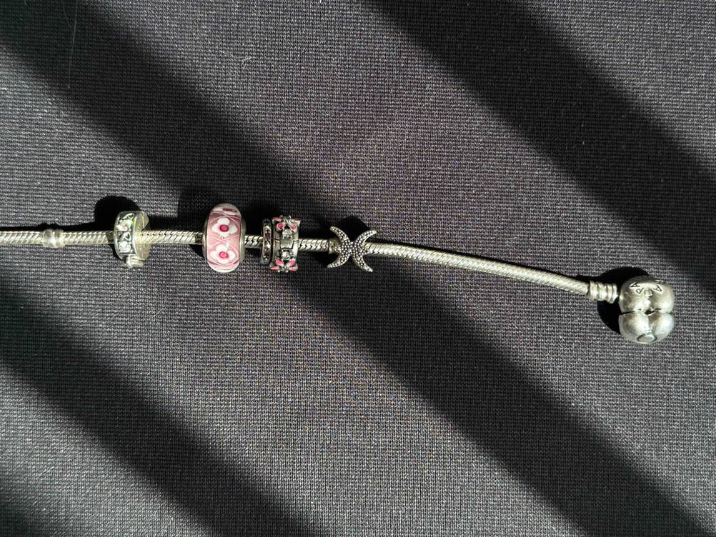 Nahaufnahme der Elemente eines getesteten Pandora-Armbands mit geöffnetem Verschluss auf einer dunklen Fläche.