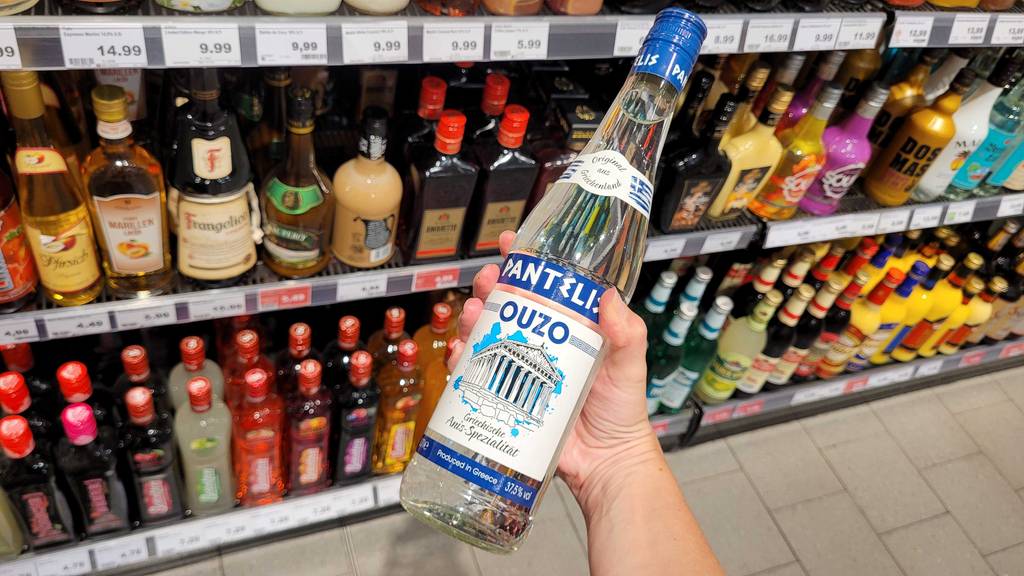 Hand hält eine Flasche Pantelis Ouzo zum testen vor einem Verkaufsregal.