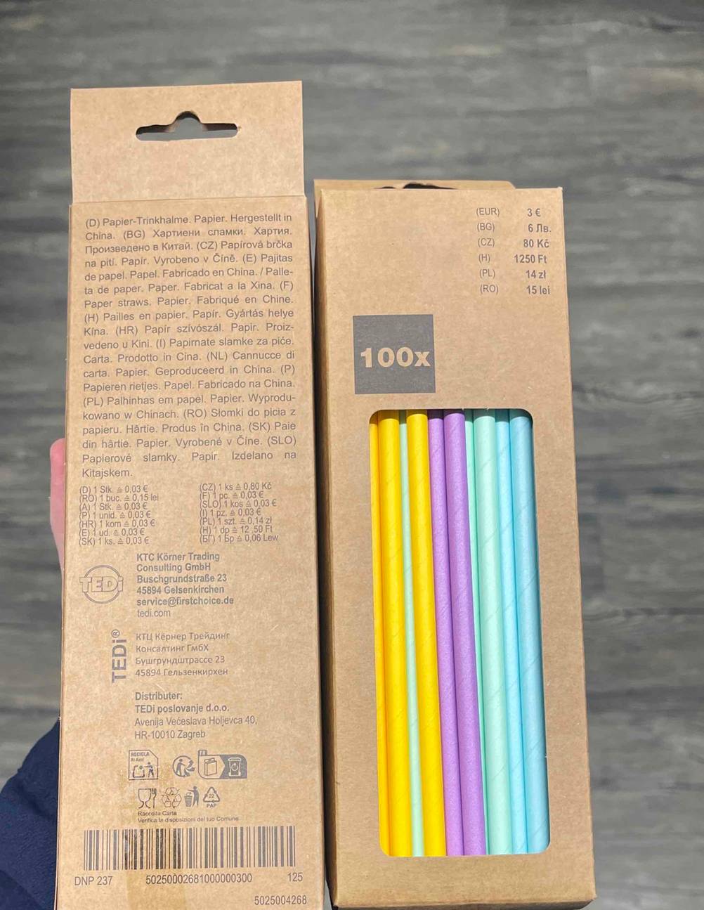 Getestet: Eine Hand hält zwei Packungen der Papierstrohhalme einmal Vorderseite nach vorne, einmal Rückseite nach vorne.