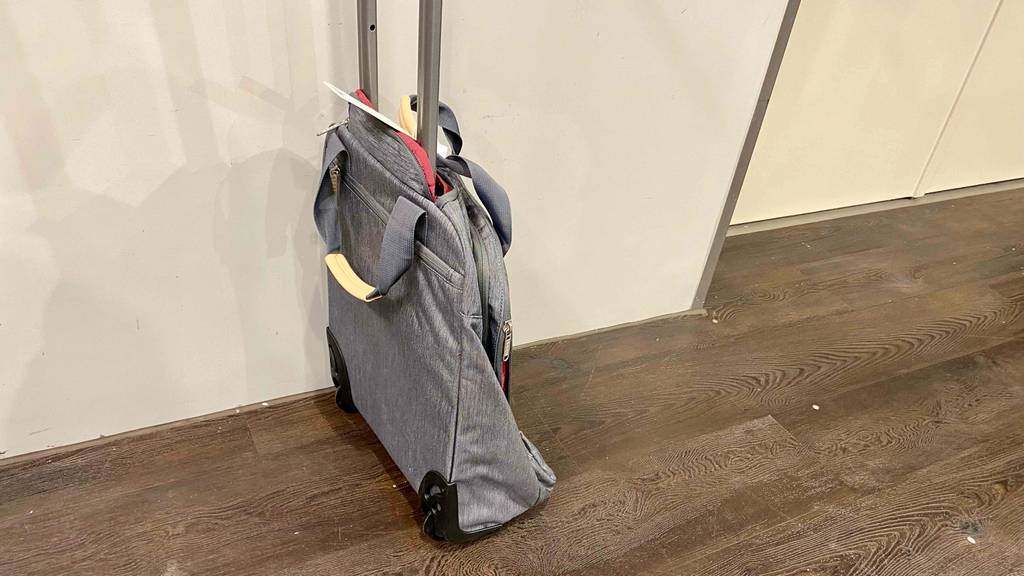 Im Test: Ein Rucksack-Trolley steht seitlich mit ausgezogenem Griff vor einer weißen Wand auf einem dunklen Holzboden.