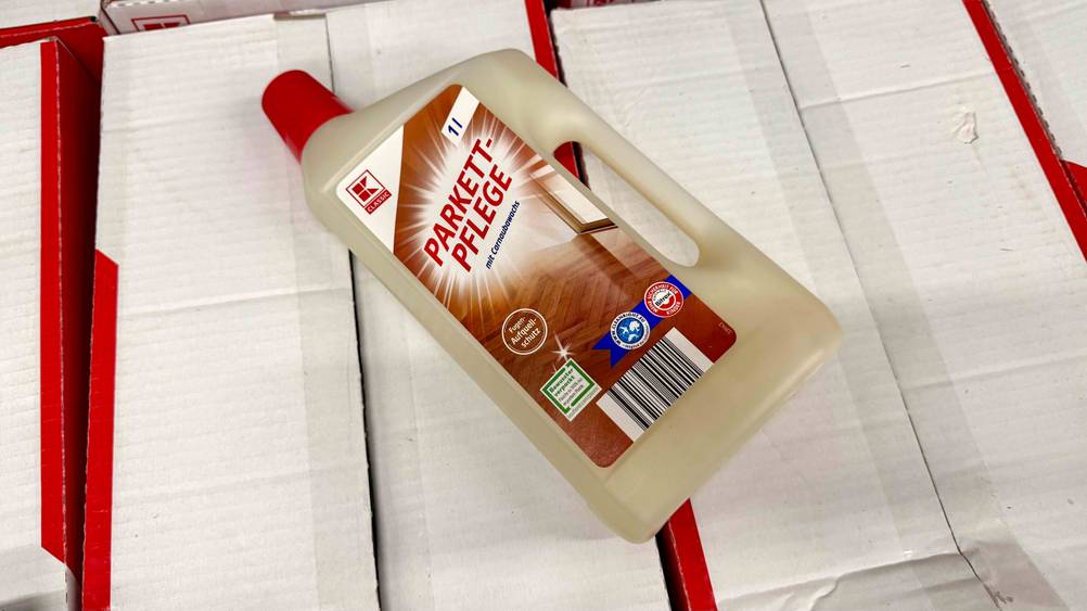 Eine Flasche der getesteten Parkettpflege liegt auf weißen Kartons.