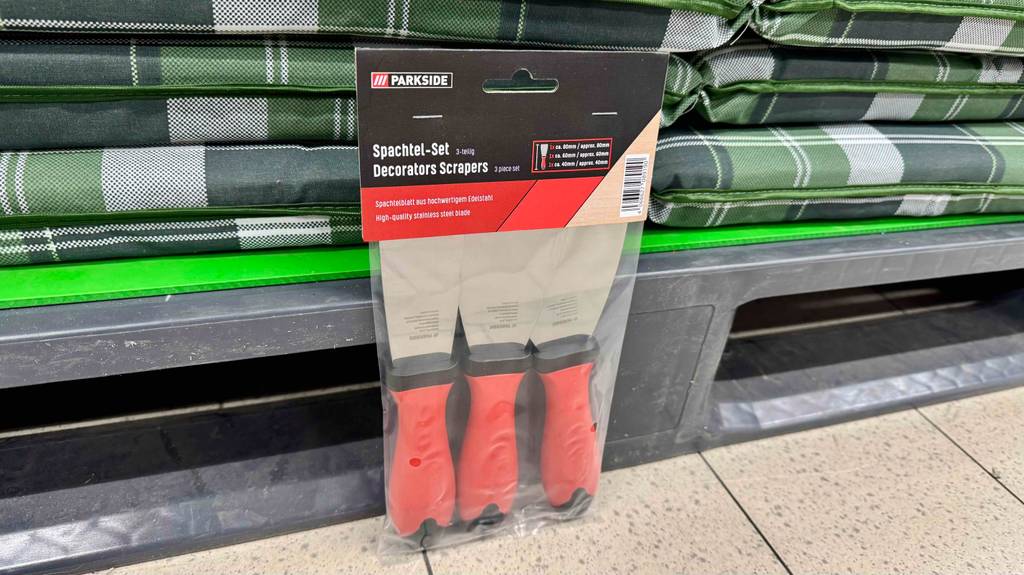 Spachtel-Test: Drei original verpackte Spachtel mit orangem Griff stehen vor einem Verkaufsregal.
