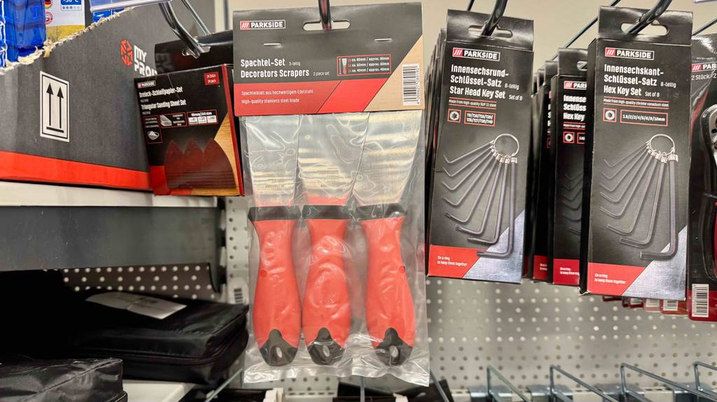 Im Test: Spachtel mit orangem Griffen hängen erhältlich im 3-er-Set an einem Verkaufsregal neben weiteren Werkzeugen.