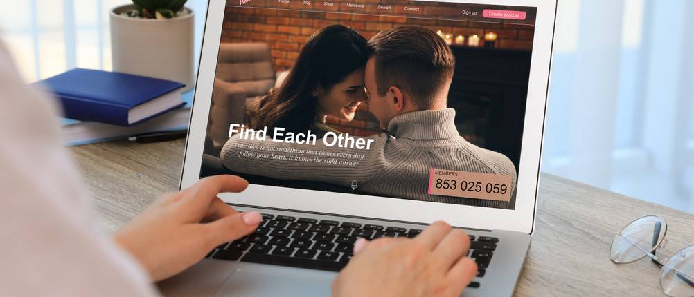 Partnersuche im Test: Eine Frau sitzt vor einem Laptop, auf dem eine Partnervermittlung geöffnet ist.