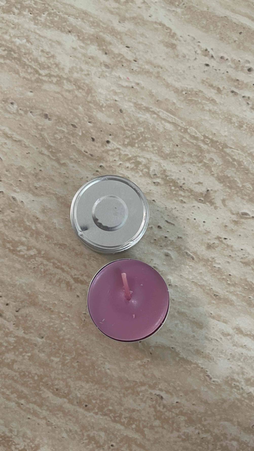 Partylite-Kerzen getestet: Ein malvenfarbiges Teelicht steht neben dem auf den Kopf gestellten Aluminiumbehälter auf einer braunen Oberfläche.