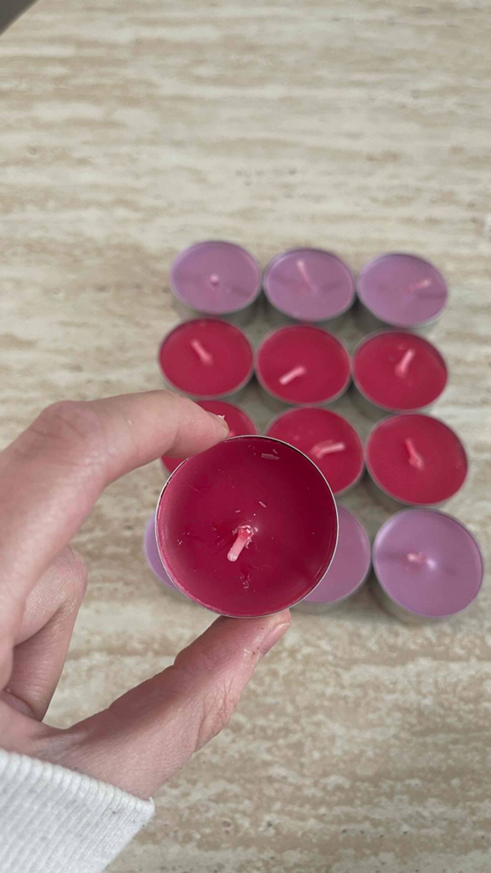 Eine Hand hält eine Partylite-Kerze im Test über mehreren malvenfarbigen und roten Teelichtern.