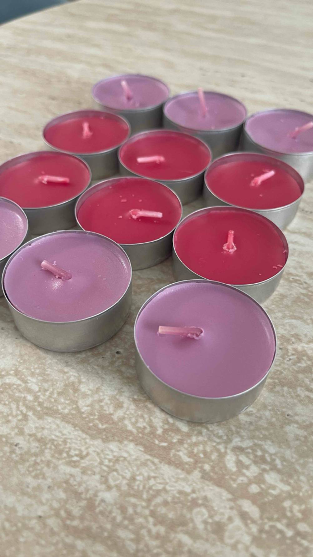 Partylite-Kerzen-Test: Sechs malvenfarbige und sechs rote Teelichter stehen geordnet auf einer braunen Oberfläche.