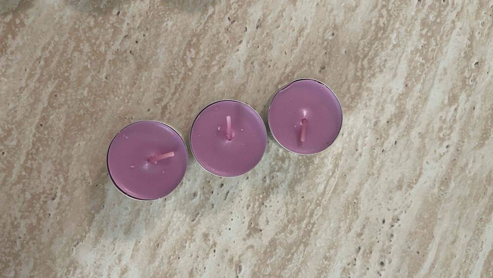Partylite-Kerzen im Test: Drei malvenfarbige Teelichter stehen in einer Reihe auf einer braunen Oberfläche.