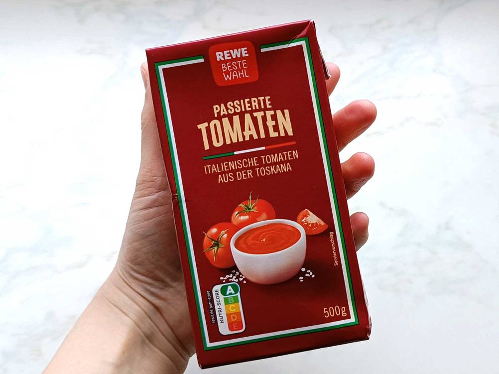 Passierte Tomaten getestet: Eine Hand hält eine Packung vor eine helle Fläche.