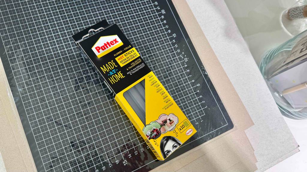 Eine Packung Heißklebesticks 11 mm liegt zum testen auf einem Schneidebrett.