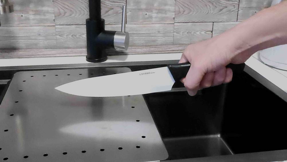 Eine Hand hält ein Paudin-Messer im Test über ein dunkles Waschbecken.