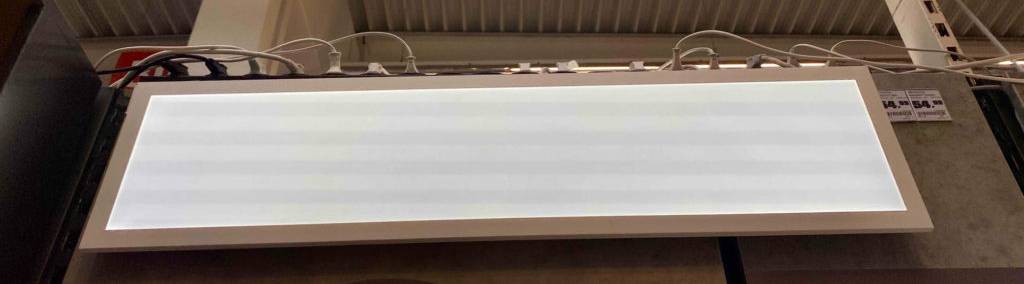 Ein rechteckiges LED-Deckenpanel im Test, mit weißem Rahmen und Milch-Glasscheibe, hängt inklusive Preisinformation in einem Verkaufsbereich.