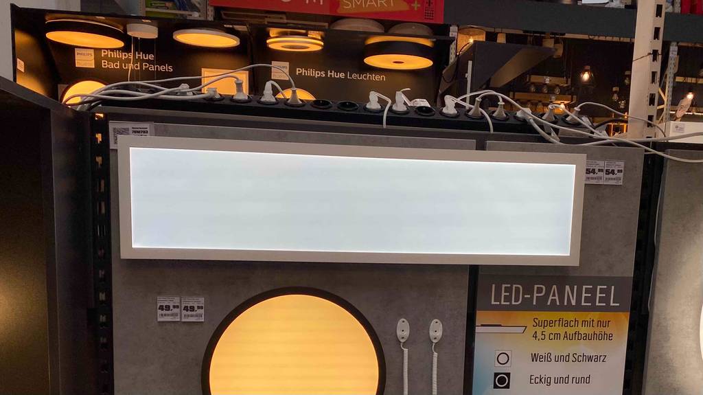 LED-Deckenpanel im Test: eine rechteckige Deckenleuchte mit matter Verglasung hängt inklusive Preisschild an einer Ausstellungswand, umgeben von runden, kleineren Decken- und Wandleuchten.