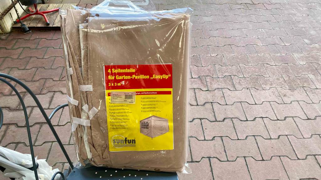 Ein Pavillon im Test: Ein einfach verpackter Pavillon befindet sich verpackt auf einem Gartenstuhl. 