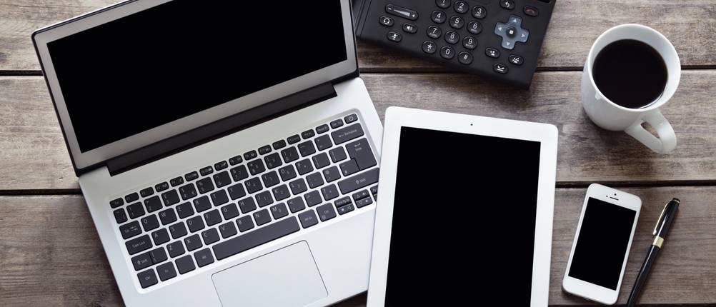 Laptop, Tablet und Smartphone liegen von oben fotografiert auf einem Holztisch