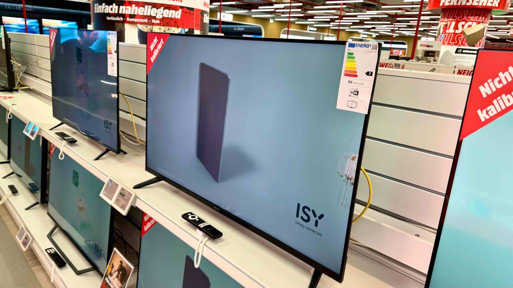 Vor einem Fernseher bis 300 Euro im Test liegt die Fernbedienung auf einem weißen Regal.