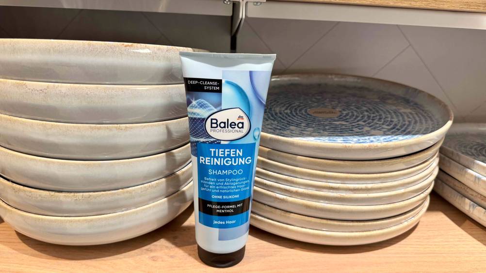 Ein Peeling-Shampoo im Test vor Tellern in einem Regal.
