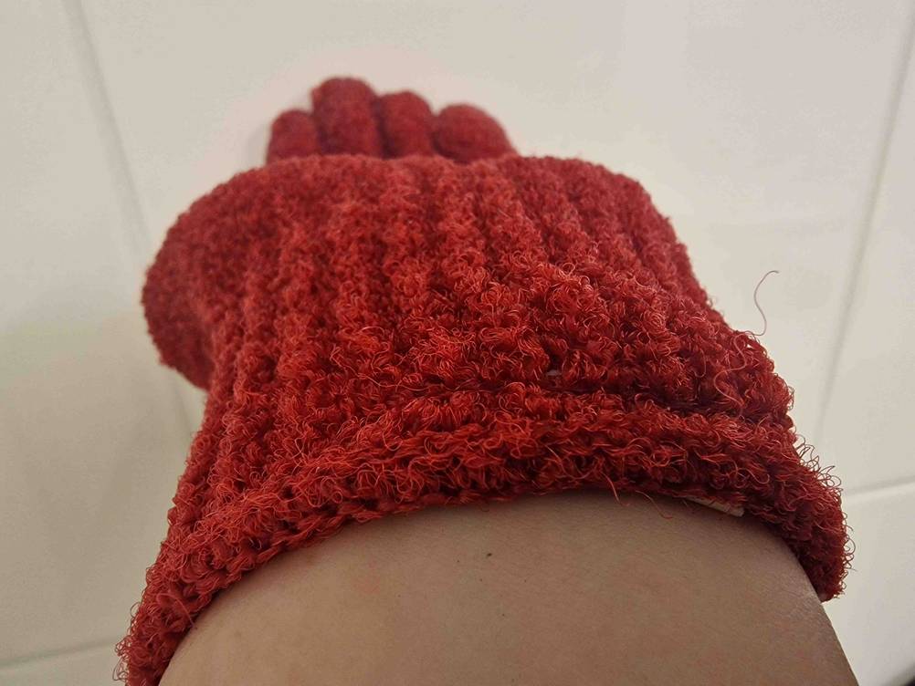 Angezogener, getesteter Peelinghandschuh in Rot, mit Fokus auf die Beschaffenheit des Materials.