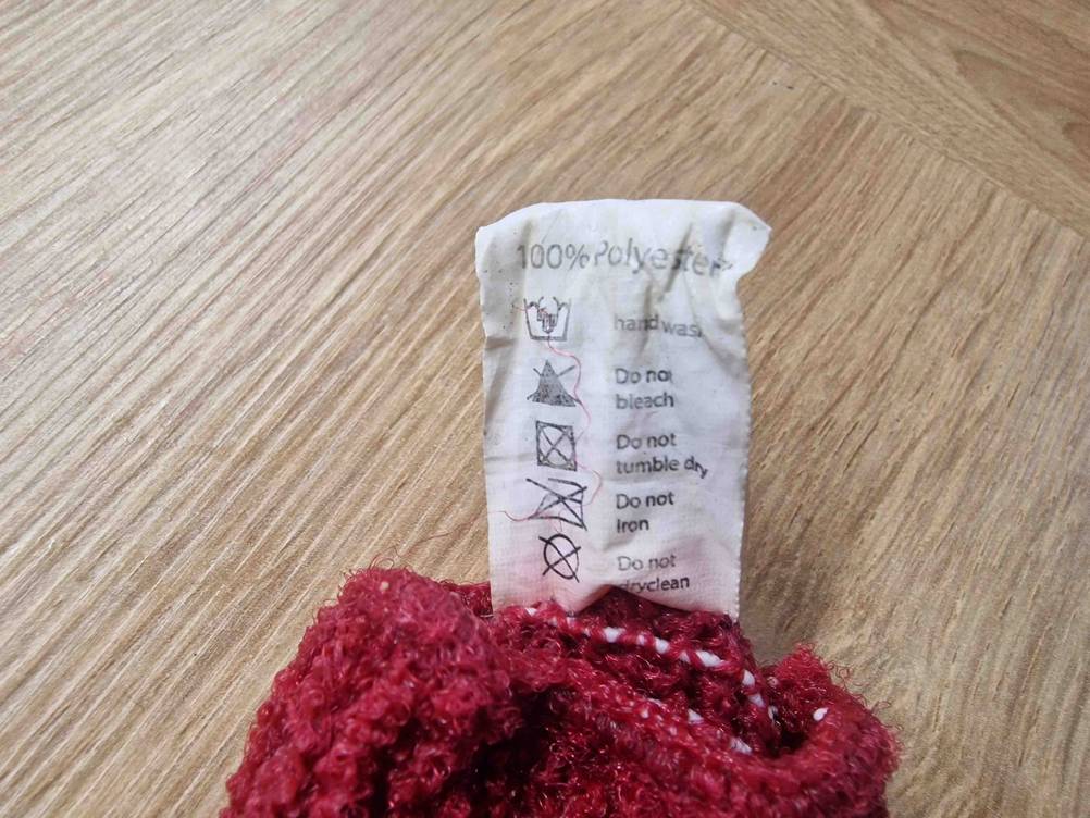 Peelinghandschuhe im Test: Detailaufnahme eines roten Peelinghandschuhs auf Holzmaserung-Untergrund, mit Fokus auf das Material-Etikett.