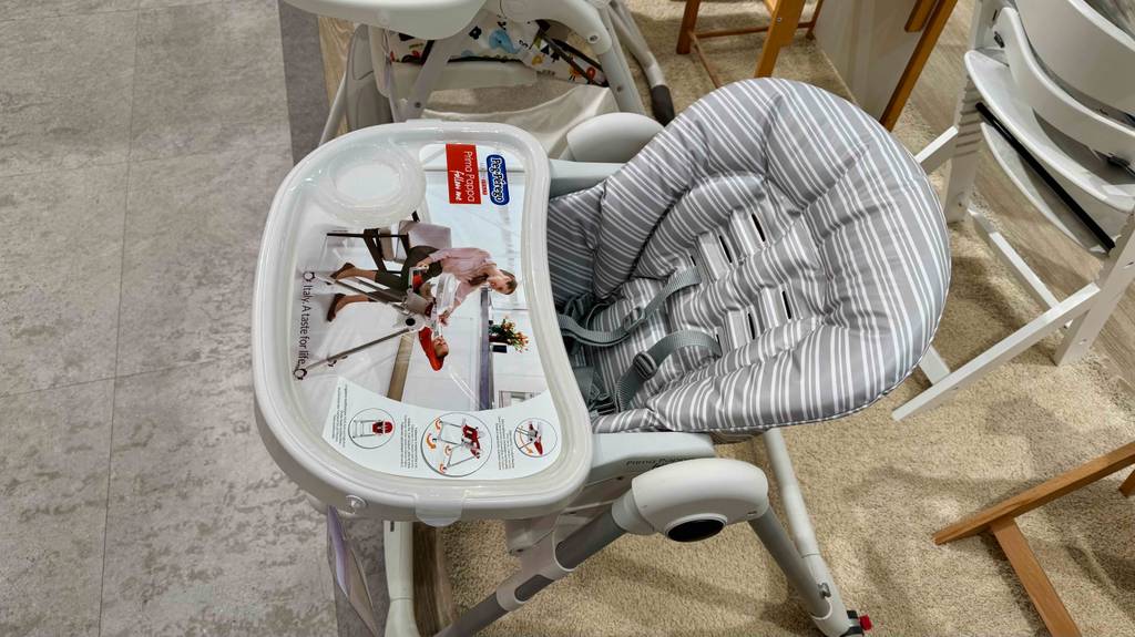 Ansicht von schräg oben auf einen getesteten Baby-Hochstuhl mit Liegefunktion, der im Verkaufsbereich zwischen weiteren Baby-Hochstühlen steht.