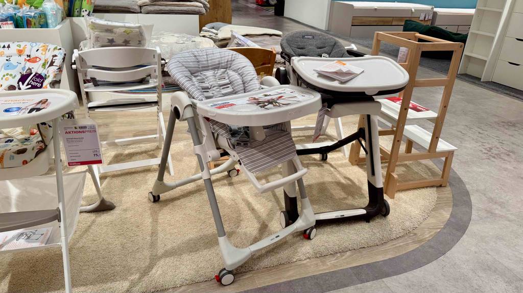 Ein Baby-Hochstuhl mit Liegefunktion im Test steht neben einem weiteren Hochstuhl auf Rollen.