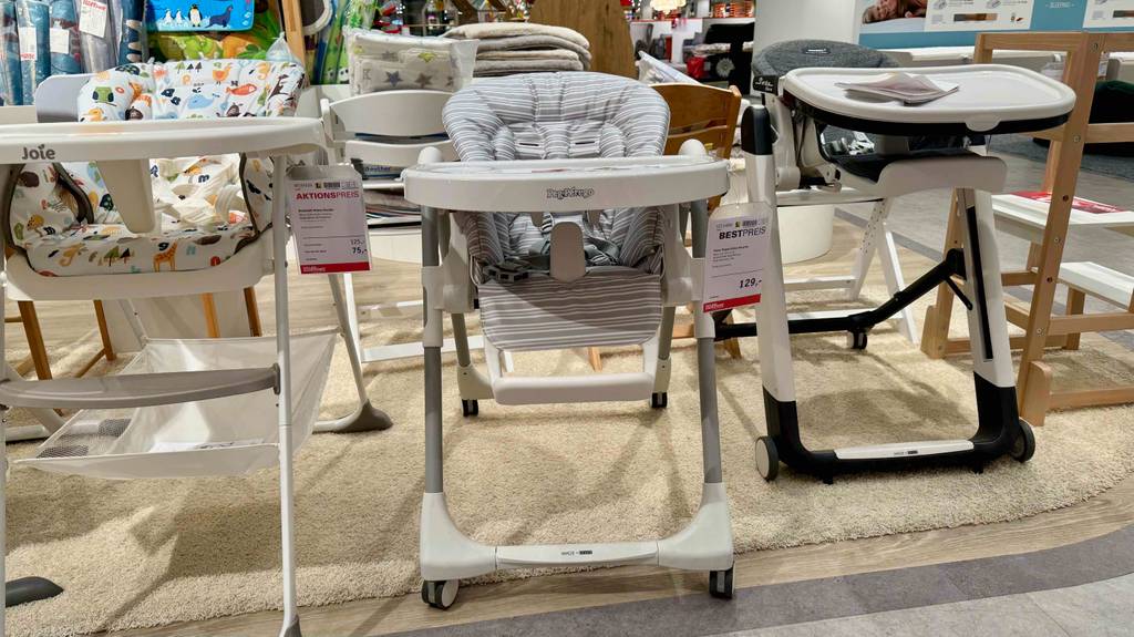 Ein Baby-Hochstuhl mit Liegefunktion im Test steht von vorn betrachtet zwischen Baby-Hochstühlen im Geschäft.