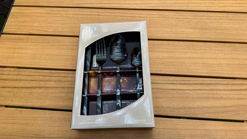 Ein schwarzes Besteck im Test liegt sichtbar in der Verpackung auf einer Holzoberfläche.