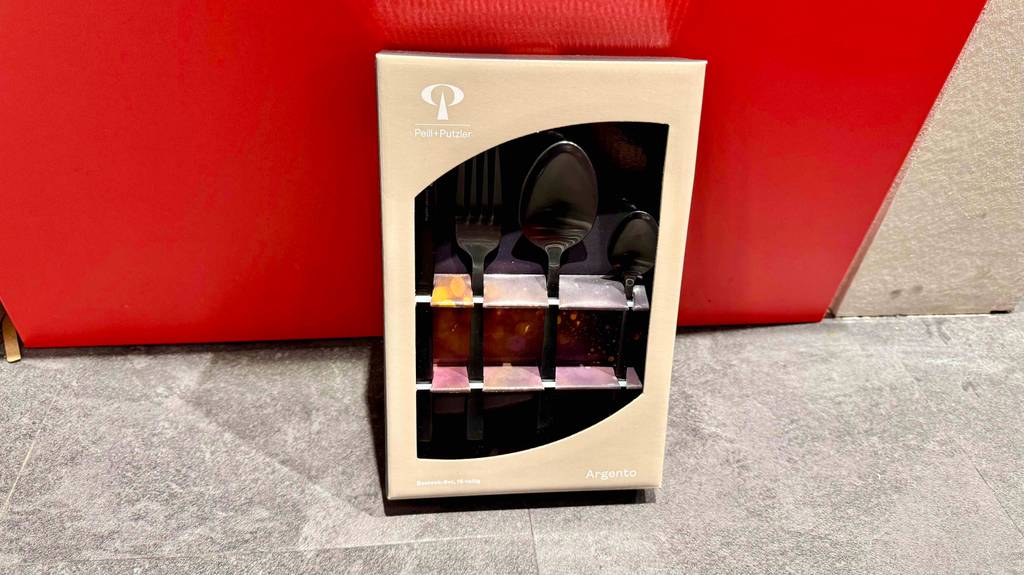 Getestet: Ein schwarzes Besteck, sichtbar in der Verpackung, lehnt an einem roten Hocker.