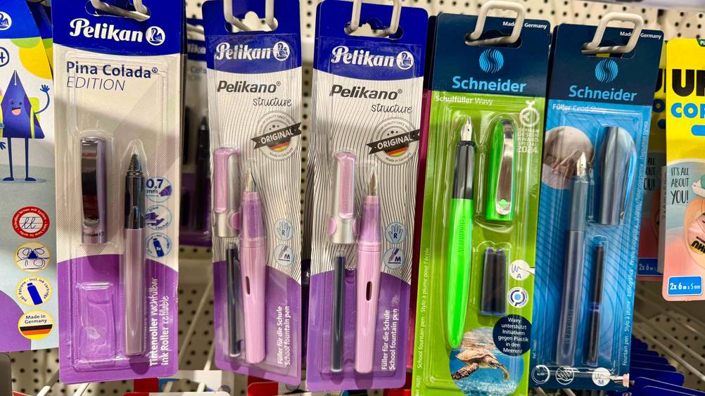 Mehrere verpackte Pelikan-Füller im Test hängen in einem Verkaufsregal neben anderen Herstellern.