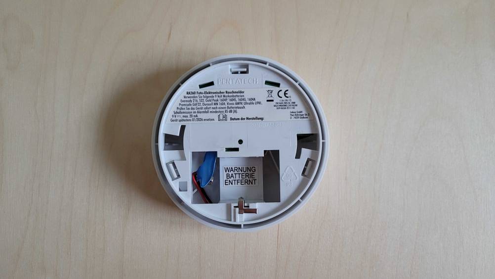 Rauchmelder-Test: Rückseite des Gerätes mit offenem Batteriefach auf einer Holzfläche.